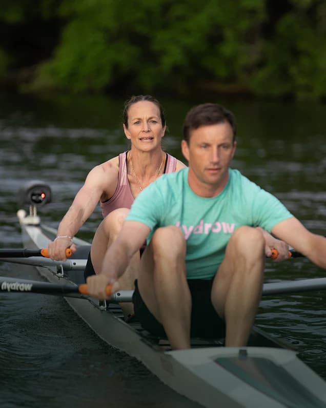 Two Hydrow athletes crouching at the water’s edge beside a shell