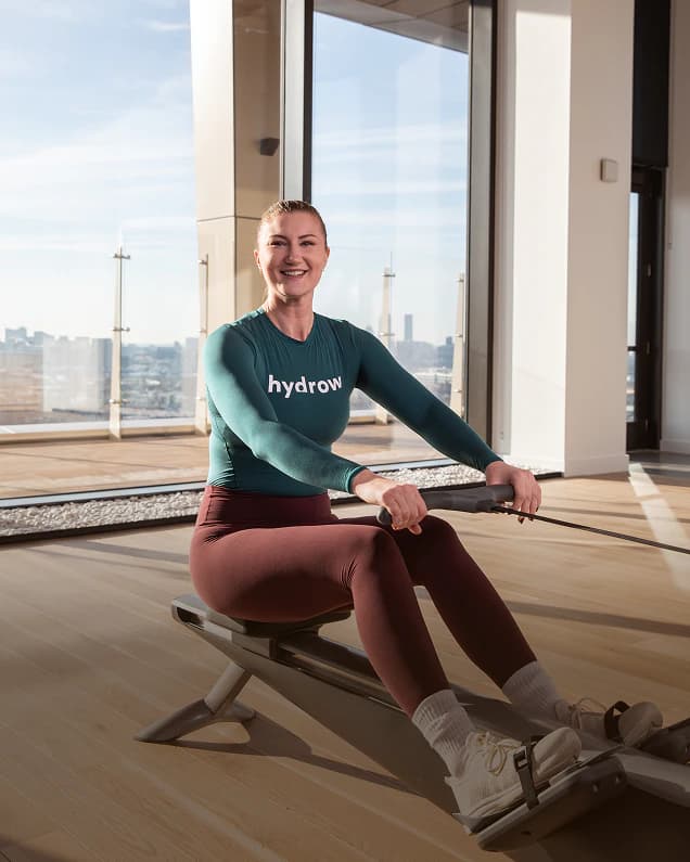 A Hydrow member rowing beside a bright window at home