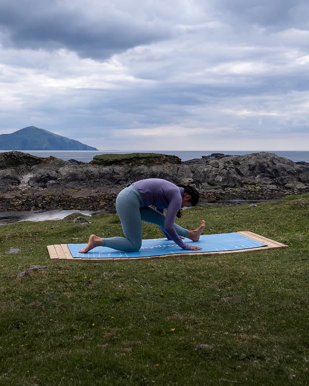 A Hydrow member stretching on a mat on the grass by the water