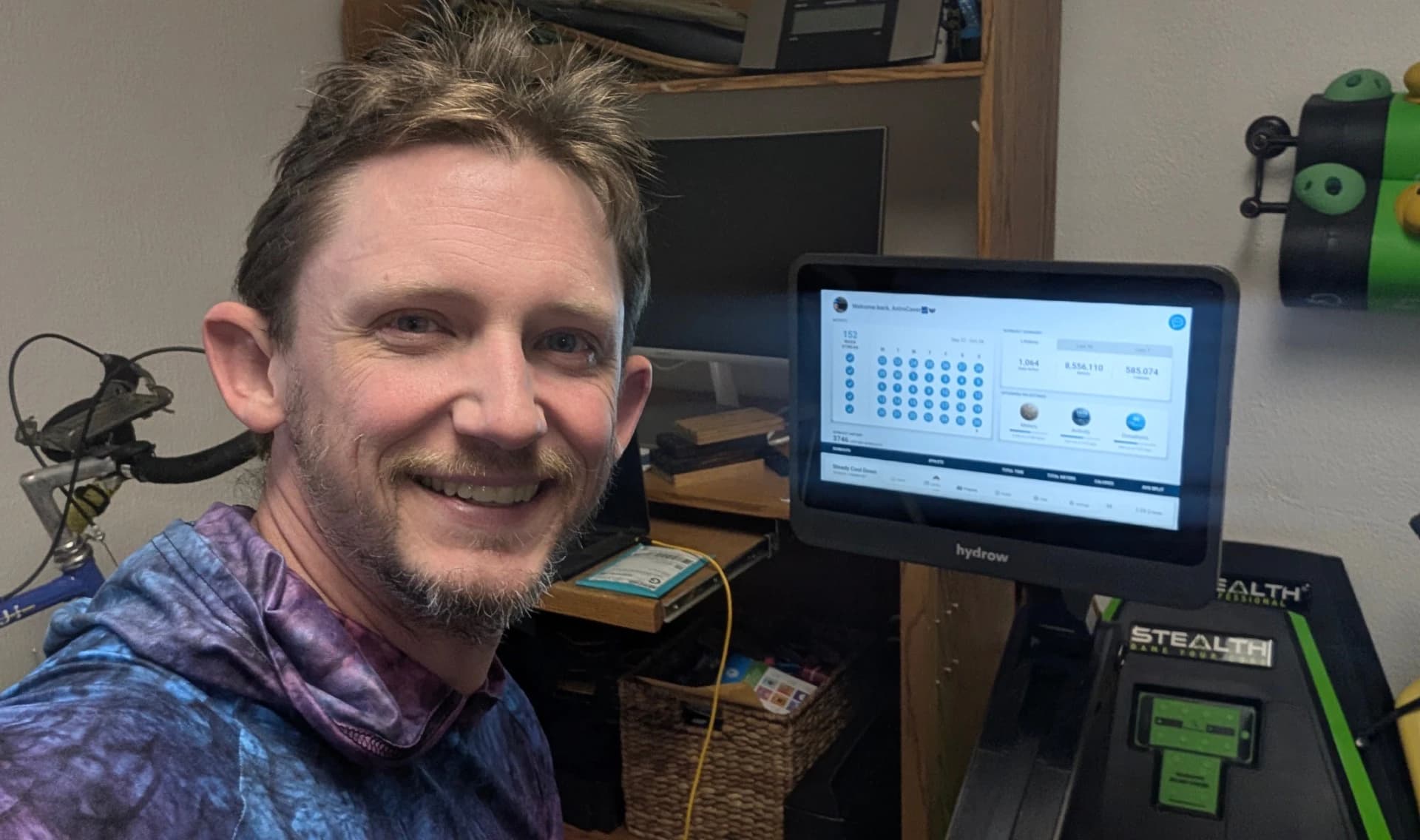 Hydrow Member Joshua Sebree smiling beside the HydroMetrics-enabled screen on his Hydrow rower