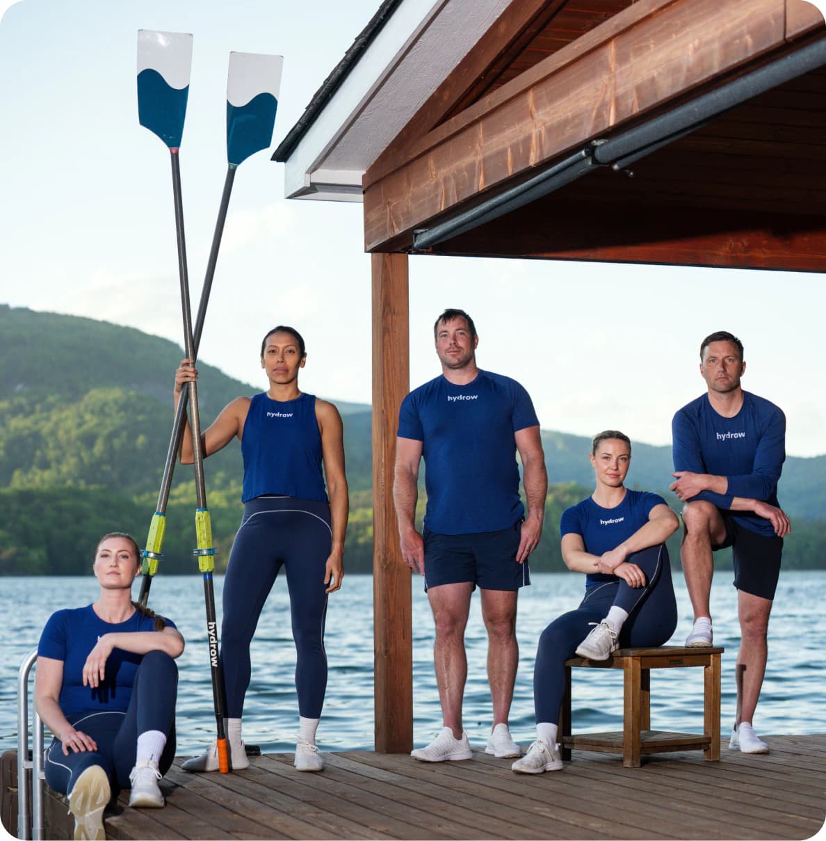 The Lake Lure crew standing on a boat dock with oars, with the lake and mountains behind them