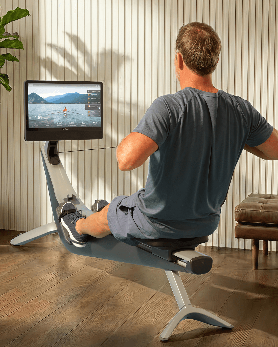 A person rowing on a Hydrow rower in a sunlit home with wood-paneled walls