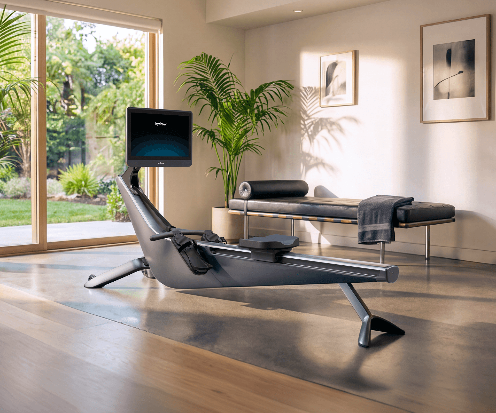Hydrow Origin rower with its screen on, in a sunlit, modern living room overlooking a lush garden.