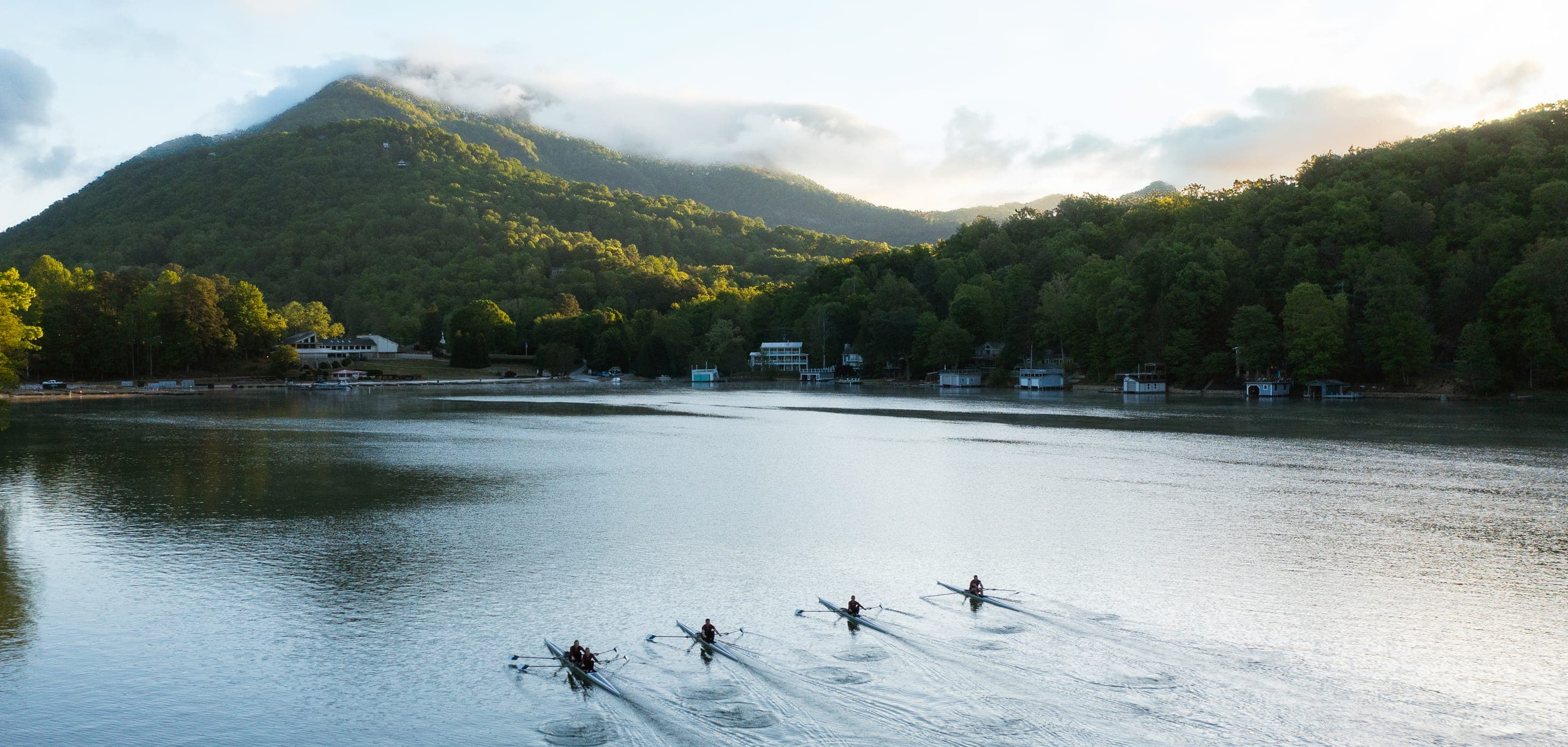 Rowers gliding across a calm lake at the base of forested mountains