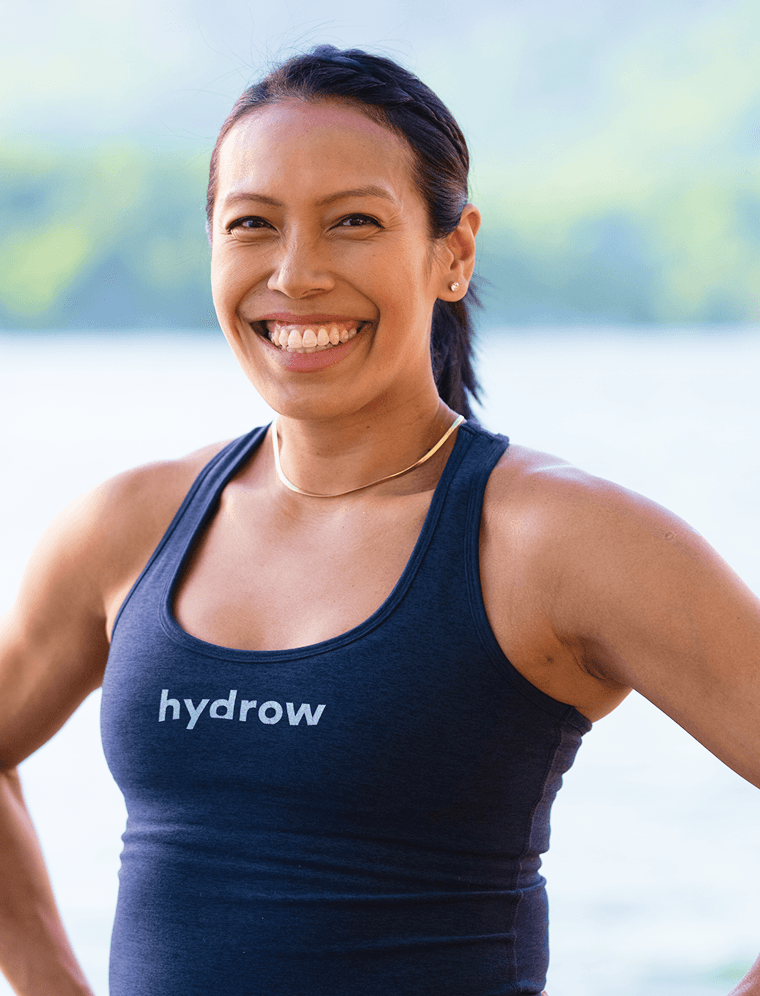 Hydrow athlete Aisyah Rafaee standing outdoors in a Hydrow tank top by the water