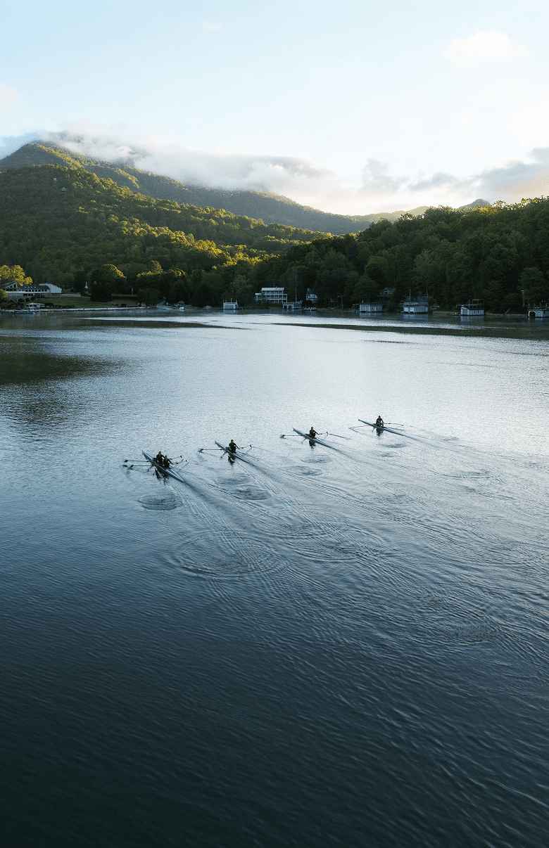 Rowers gliding across a calm lake at the base of forested mountains