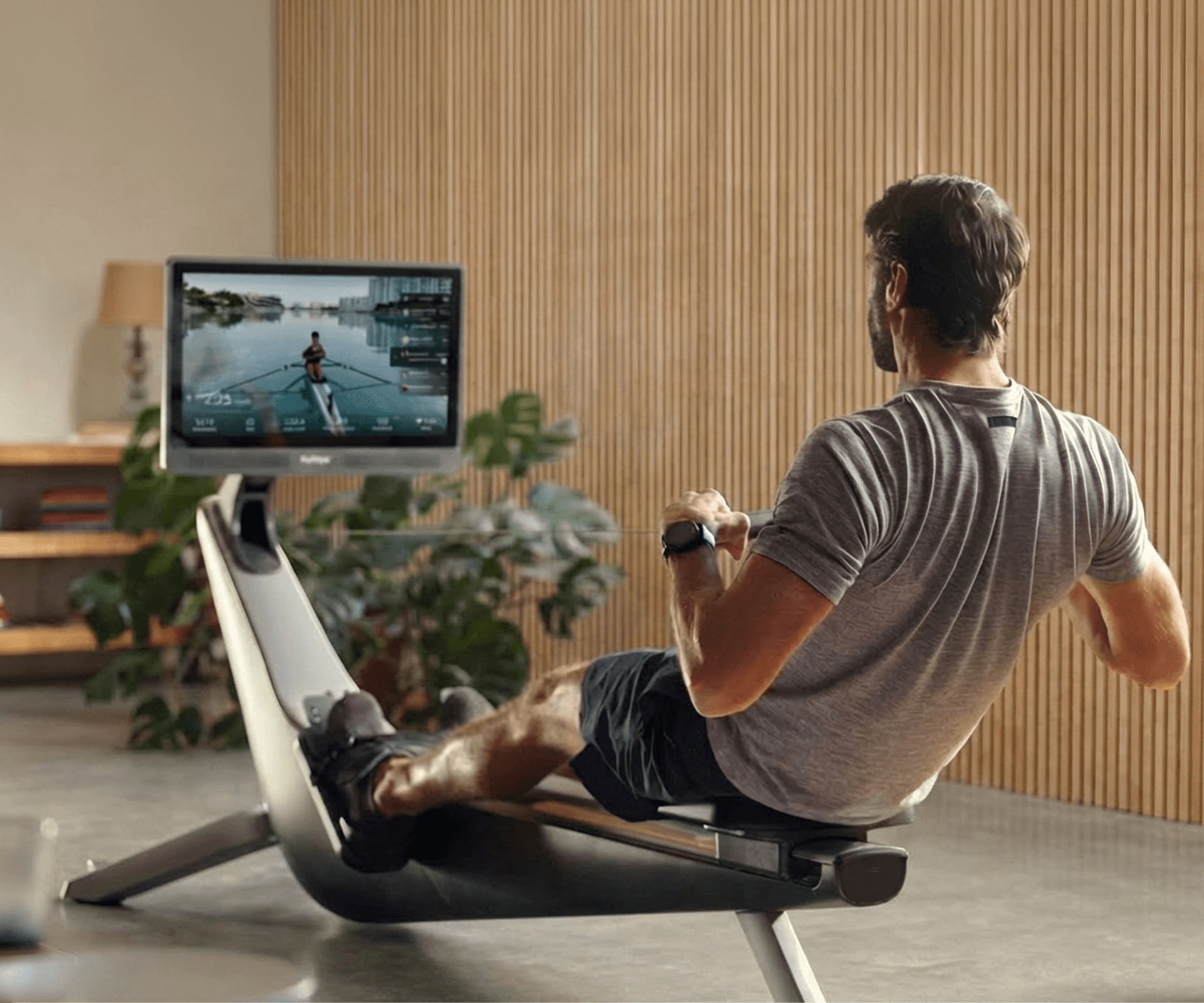 A person rowing on a Hydrow Origin machine, watching an on-water workout on the screen.