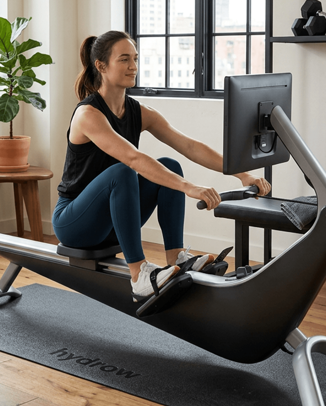 A person rowing on a Hydrow rower in a sunlit room